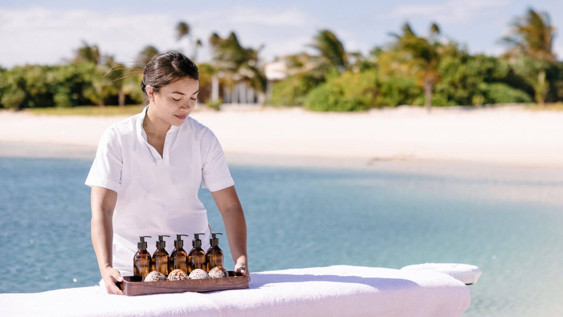 Therapist placing essential oils next to a massage bed overlooking the ocean at Miavana , Madagascar