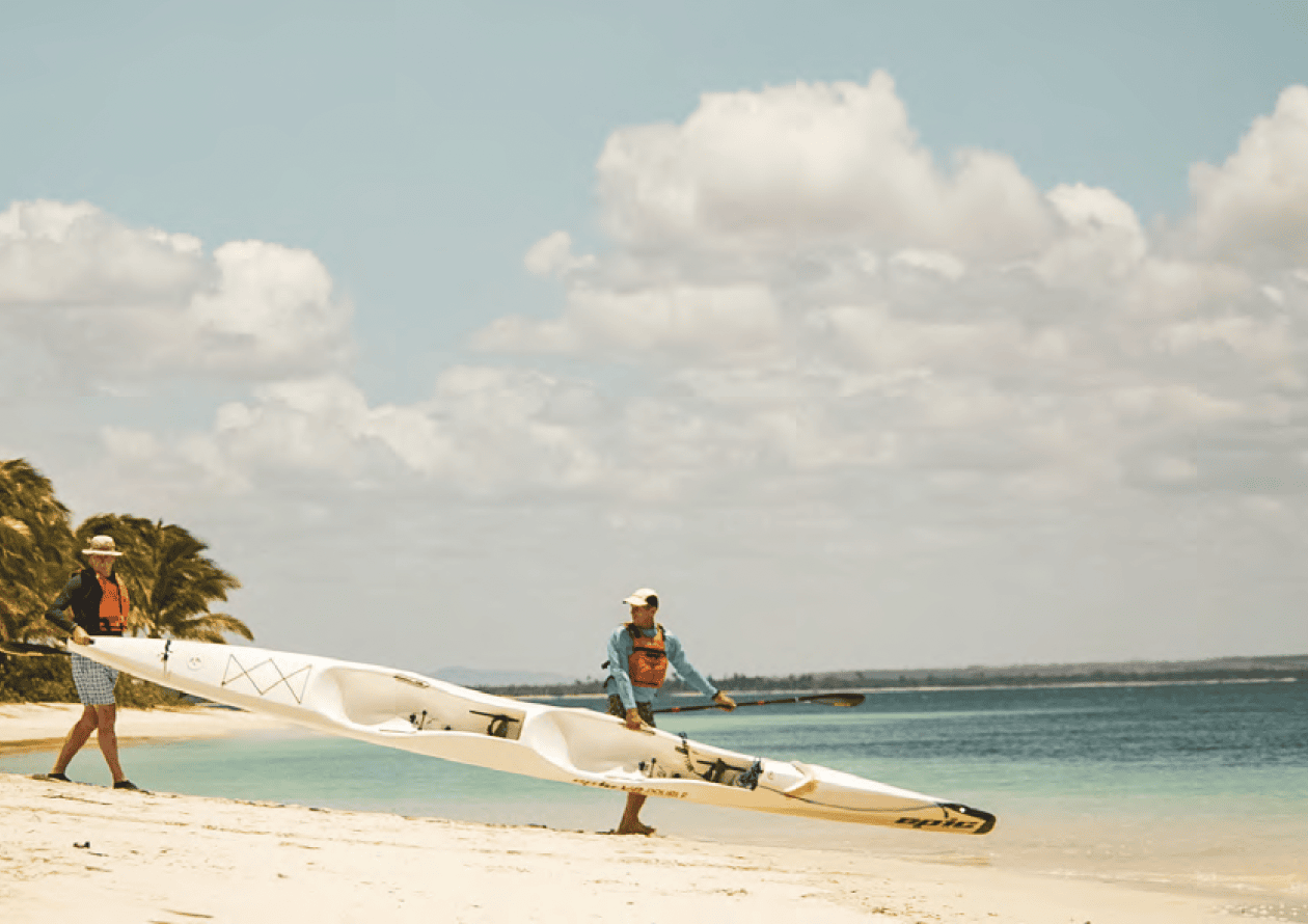 Surfski Dawid Mocke A guest and a guide carrying a sea kayak towards the ocean at Miavana by Time + Tide in Madagascar